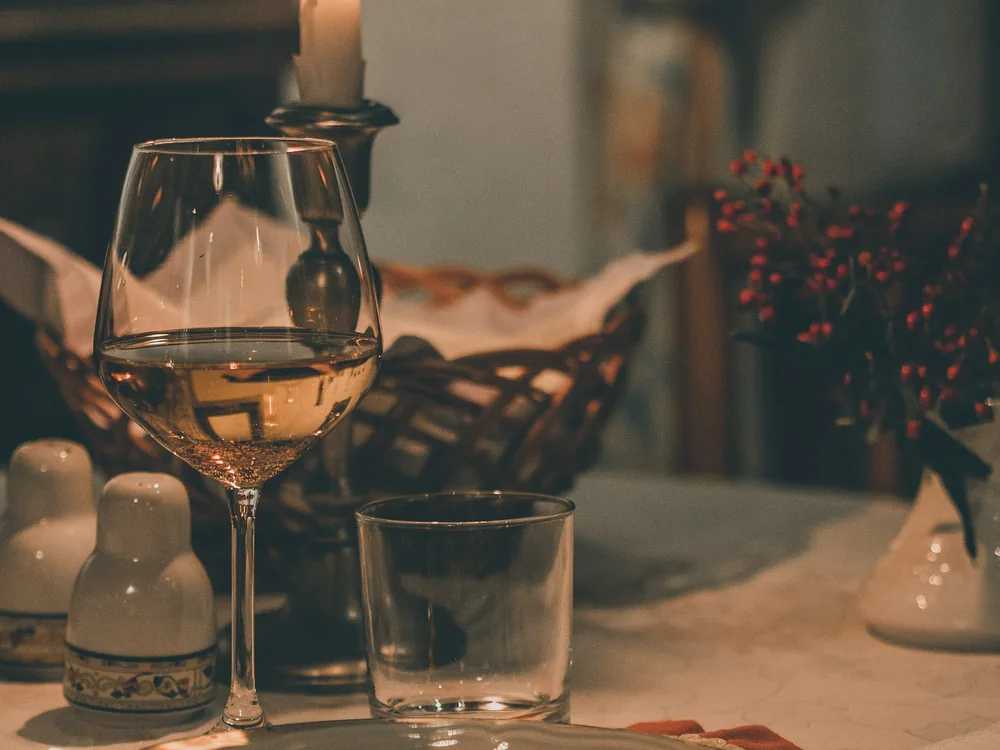 A glass of white wine beside a lit candle at a dinner table
