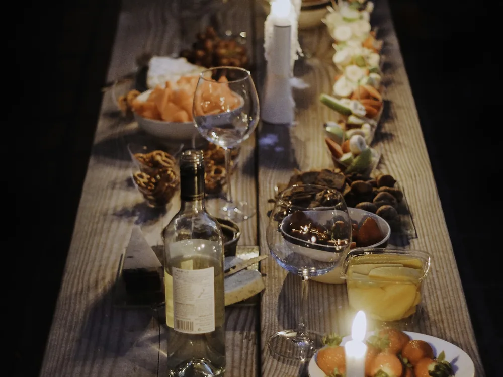 A long wooden table set with wine, bread and small dishes by candlelight